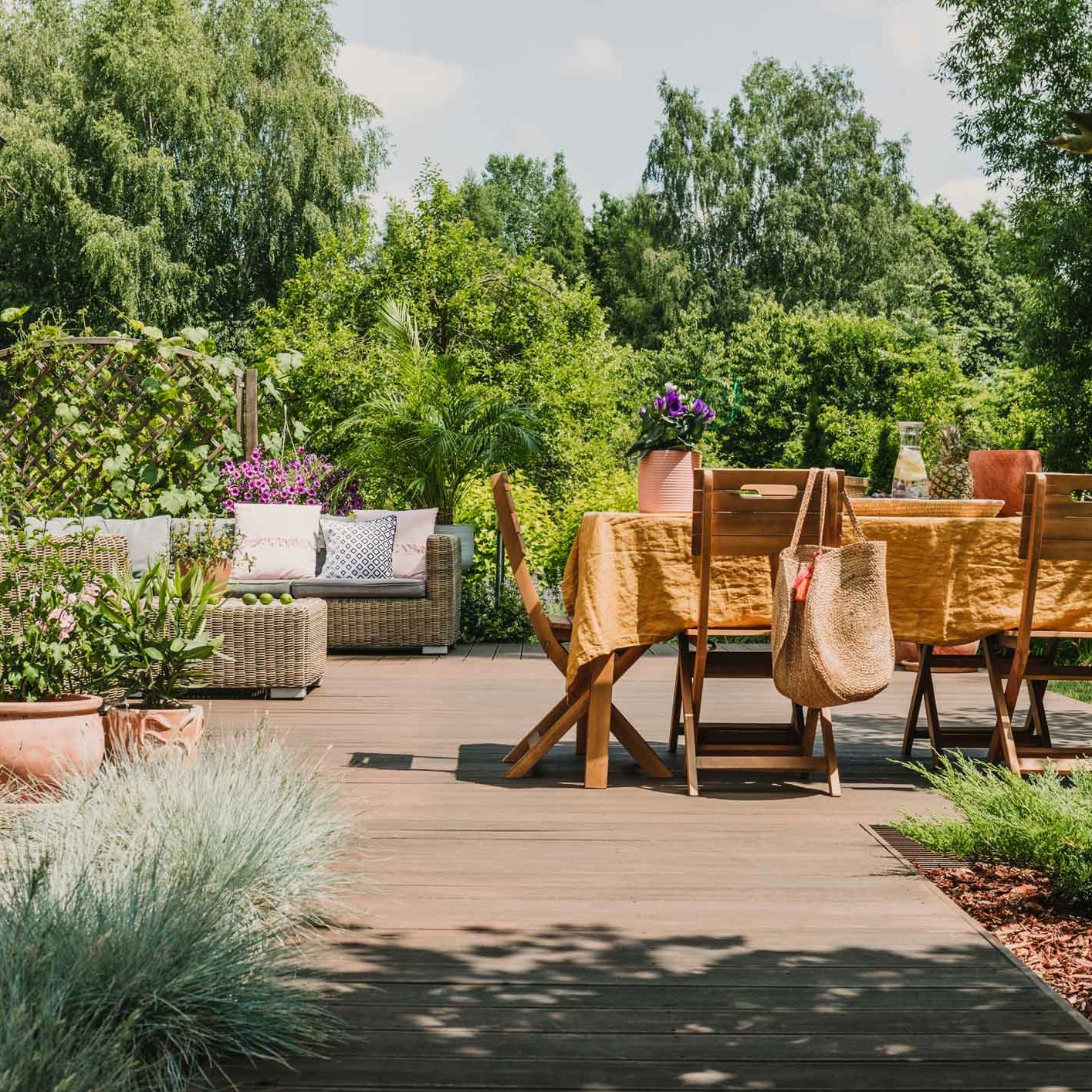 Machen Sie es sich gemütlich - auf einer Holzterrasse. Gartenmöbel aus Holz stehen auf Holzterrasse in einem Garten mit vielen Bäumen und anderen Pflanzen